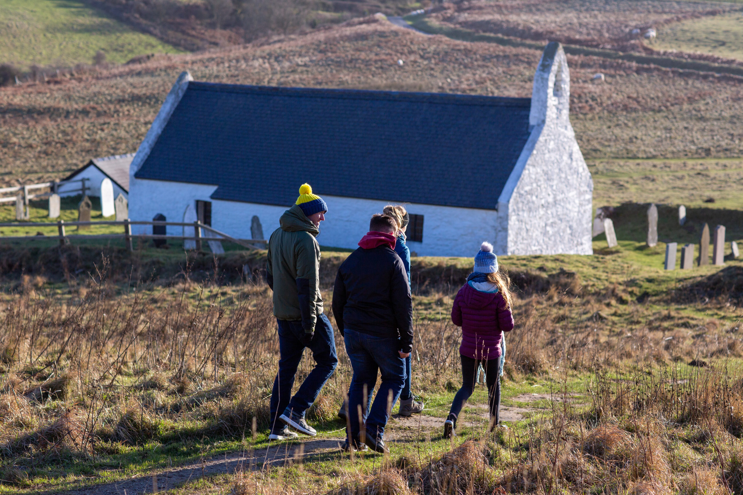 Family of four wearing winter hats and jackets, walking in the hills in Ceredigion